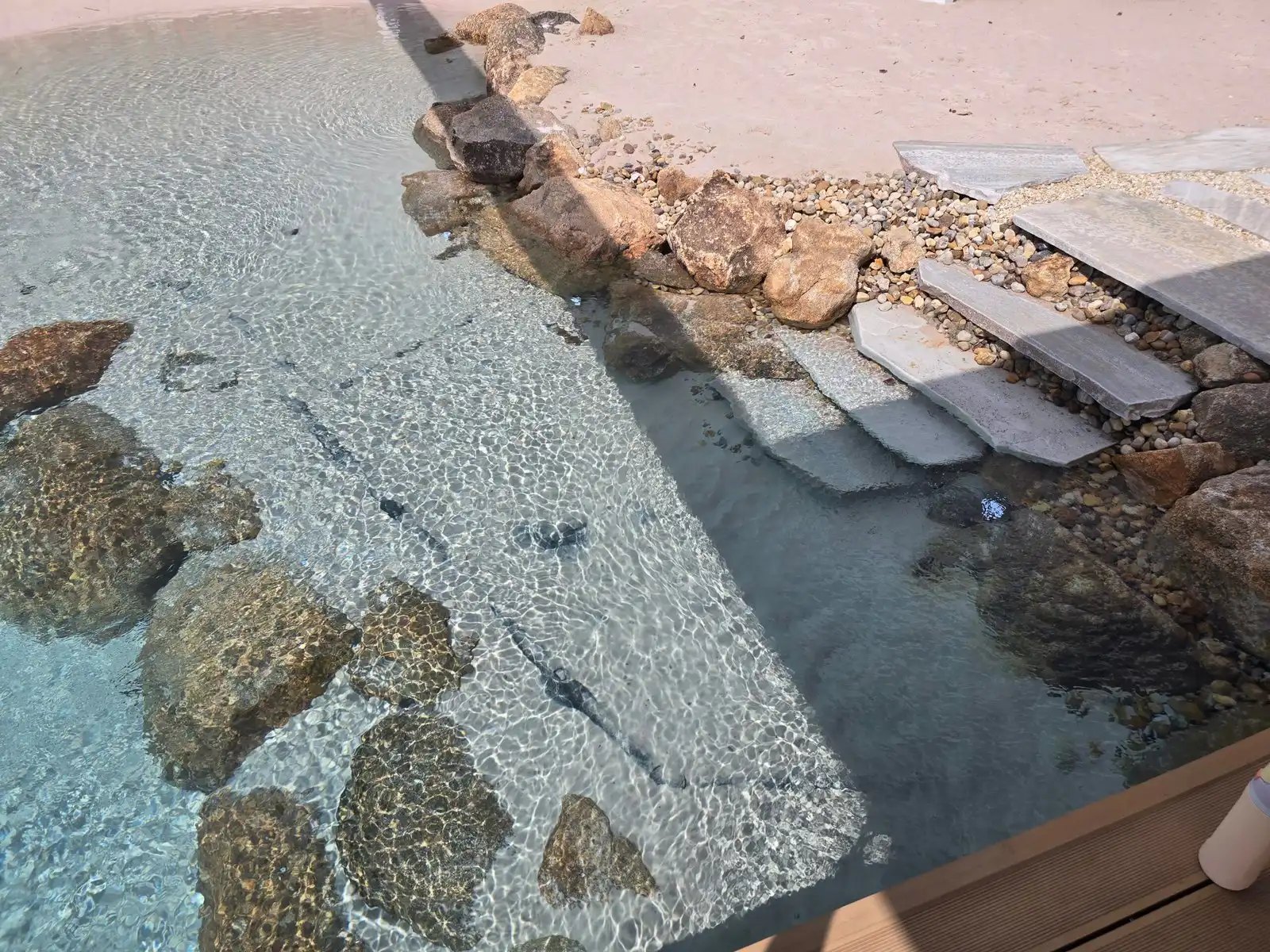 Accès piscine lagon moderne Marches en pierre plate menant à une eau turquoise limpide